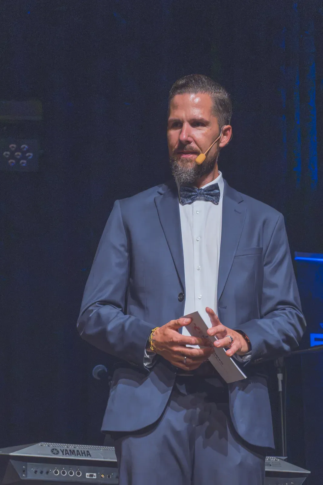 Moderator Stefan Kramberg im blauen Anzug mit Fliege auf der Bühne